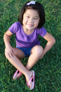 Lydia sitting in the grass, legs crossed with a big smile. 